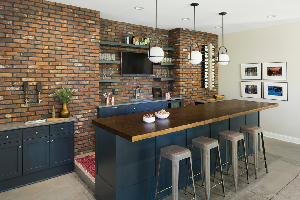 This is an example of a large beach style seated home bar in Minneapolis with shaker cabinets, blue cabinets, wood benchtops, brick splashback, concrete floors, grey floor, brown benchtop and an undermount sink.