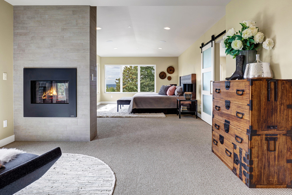 Contemporary master bedroom in Seattle with carpet, a two-sided fireplace, a tile fireplace surround and beige floor.