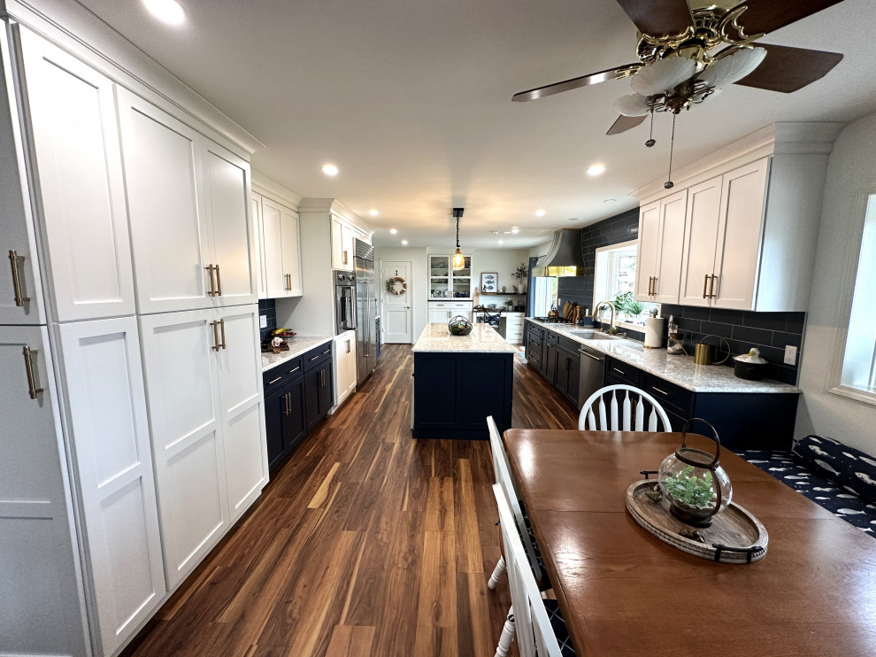 Large traditional galley kitchen/diner in Detroit with a submerged sink, shaker cabinets, white cabinets, engineered stone countertops, blue splashback, ceramic splashback, stainless steel appliances, medium hardwood flooring, an island, brown floors and white worktops.