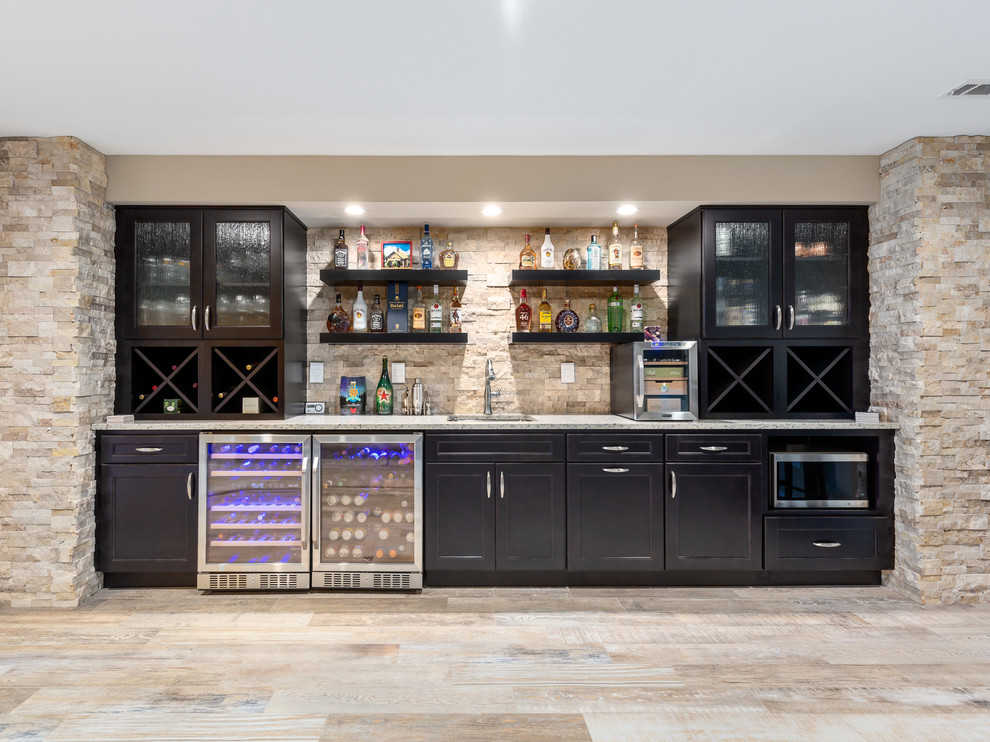 Large contemporary single-wall seated home bar in DC Metro with an undermount sink, shaker cabinets, dark wood cabinets, granite benchtops, brown splashback, travertine splashback, porcelain floors, beige floor and grey benchtop.