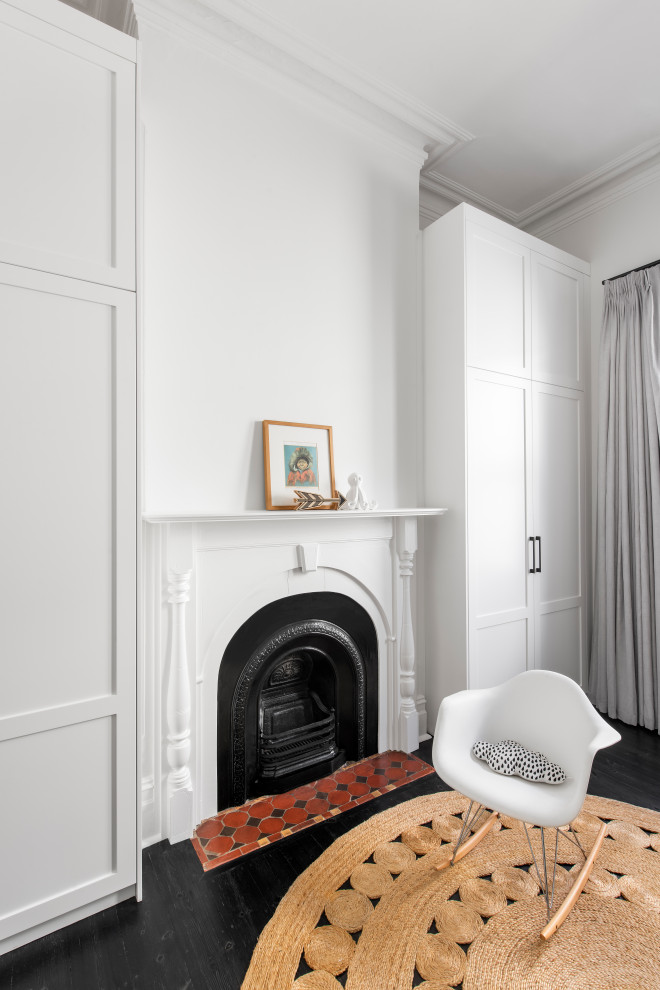 На фото: гостевая спальня среднего размера, (комната для гостей) в современном стиле с белыми стенами, деревянным полом, стандартным камином, фасадом камина из дерева, черным полом, сводчатым потолком и кирпичными стенами с