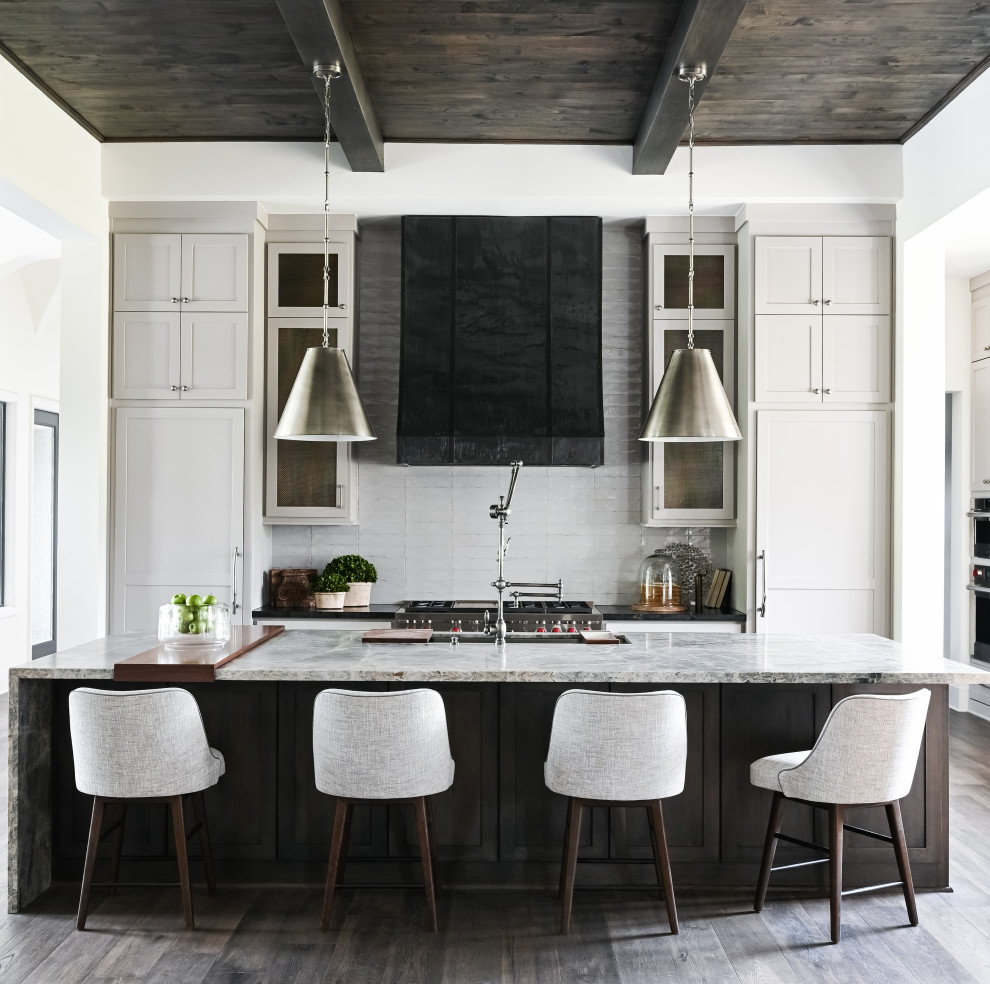 Modelo de cocina lineal, clásica renovada, de tamaño medio, abierta, con fregadero sobremueble, armarios con paneles empotrados, puertas de armario blancas, encimera de cuarcita, salpicadero verde, salpicadero de azulejos de cerámica, electrodomésticos de acero inoxidable, suelo de madera oscura, una isla, suelo marrón, encimeras grises y vigas vistas