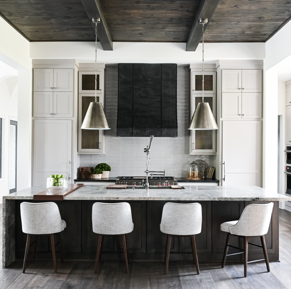 Mid-sized transitional single-wall open plan kitchen in Houston with a farmhouse sink, recessed-panel cabinets, white cabinets, quartzite benchtops, grey splashback, ceramic splashback, stainless steel appliances, dark hardwood floors, with island, brown floor, grey benchtop and exposed beam.