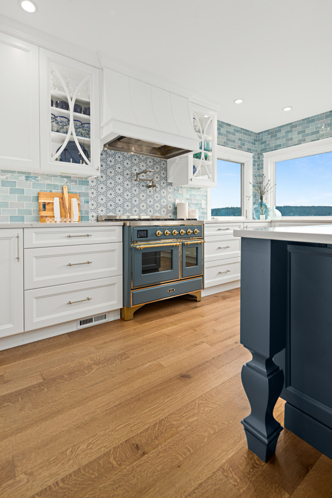 Design ideas for a large classic u-shaped kitchen/diner in Seattle with a belfast sink, recessed-panel cabinets, blue cabinets, engineered stone countertops, blue splashback, ceramic splashback, coloured appliances, medium hardwood flooring, an island, brown floors and white worktops.