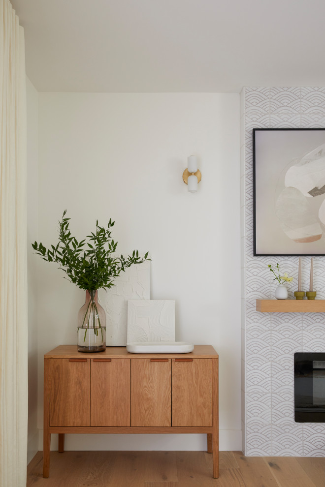 На фото: маленькая открытая гостиная комната в скандинавском стиле с белыми стенами, светлым паркетным полом, стандартным камином, фасадом камина из плитки, телевизором на стене и коричневым полом для на участке и в саду