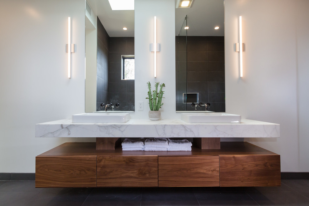 Photo of a mid-sized modern master bathroom in Los Angeles with flat-panel cabinets, dark wood cabinets, a corner tub, an open shower, a two-piece toilet, gray tile, ceramic tile, grey walls, porcelain floors, a vessel sink, marble benchtops, grey floor, an open shower and white benchtops.