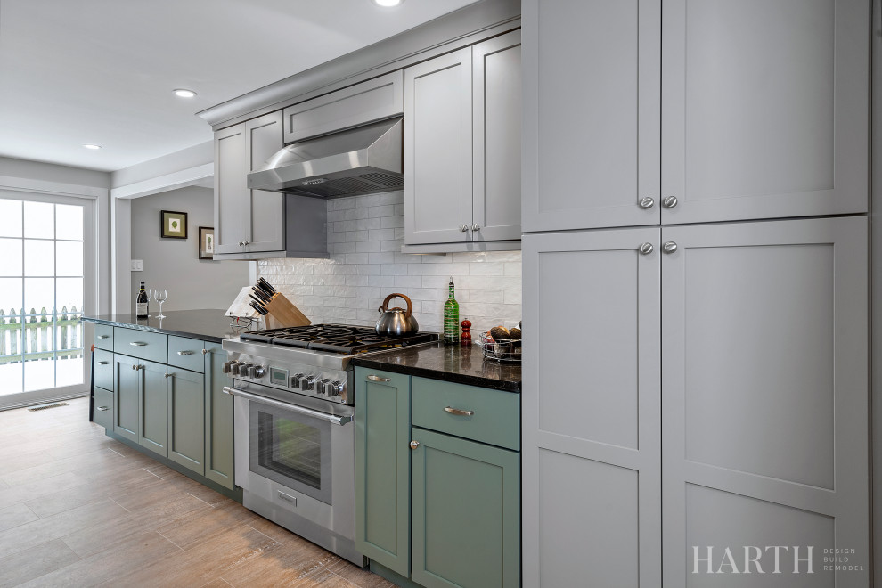 Mid-sized transitional galley separate kitchen in Philadelphia with an undermount sink, shaker cabinets, green cabinets, quartz benchtops, white splashback, porcelain splashback, stainless steel appliances, laminate floors, a peninsula, brown floor and black benchtop.