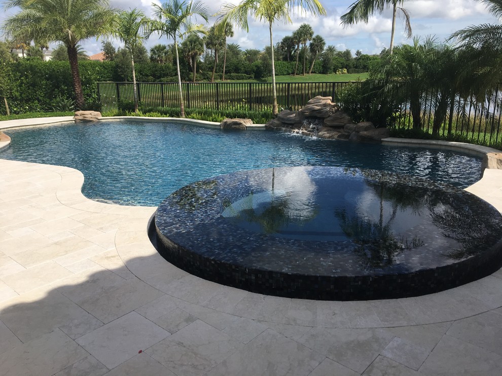 Design ideas for a large modern backyard custom-shaped natural pool in Miami with a water feature and natural stone pavers.