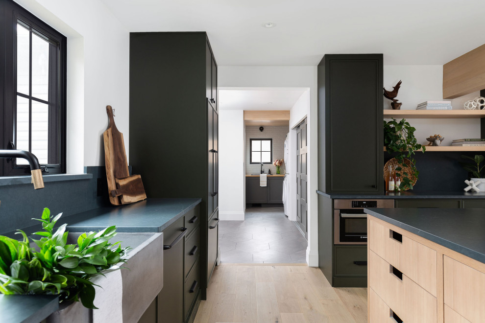 This is an example of a large contemporary u-shaped eat-in kitchen in Toronto with flat-panel cabinets, green cabinets, soapstone benchtops, white splashback, panelled appliances, with island and black benchtop.