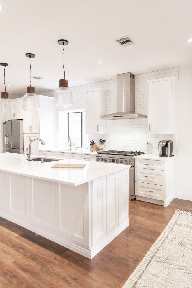 Eat-in kitchen - mid-sized transitional medium tone wood floor and brown floor eat-in kitchen idea in Phoenix with shaker cabinets, white cabinets, white backsplash, subway tile backsplash, stainless steel appliances and an island