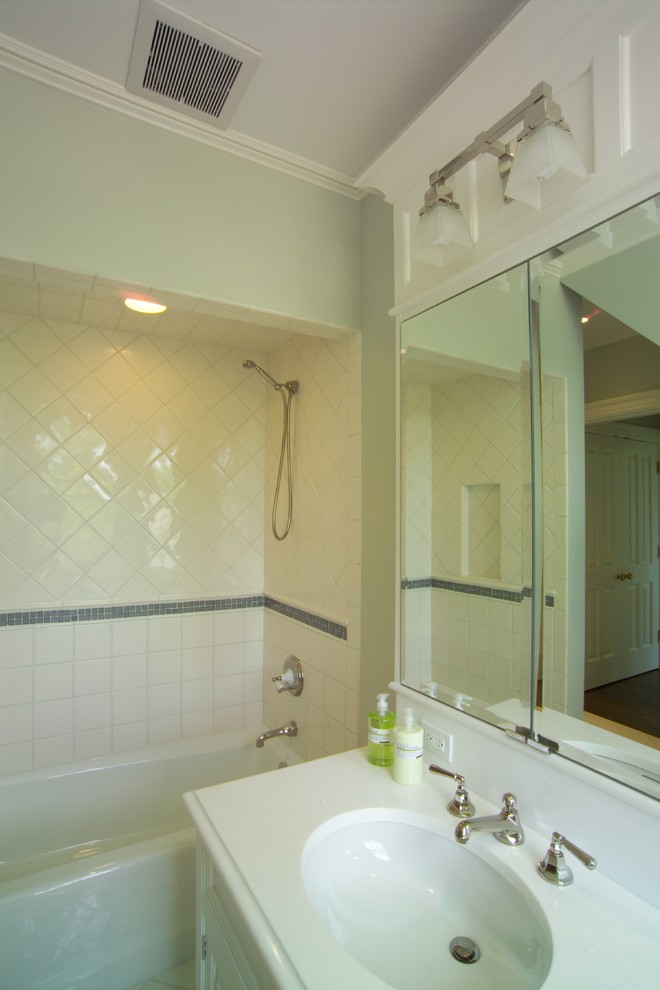 This is an example of a large traditional bathroom in New York with an undermount sink, white cabinets, solid surface benchtops, an alcove tub, a shower/bathtub combo, white tile, ceramic tile, green walls and ceramic floors.