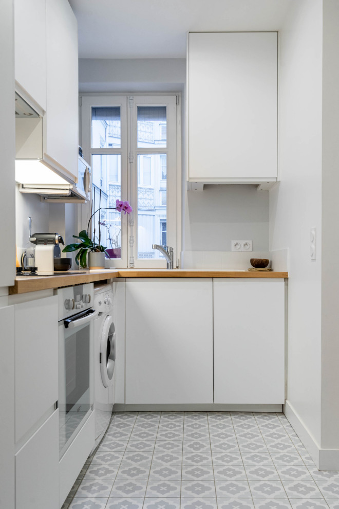 Inspiration for a small traditional grey and white l-shaped open plan kitchen in Paris with a built-in sink, flat-panel cabinets, white cabinets, wood worktops, grey splashback, ceramic splashback, white appliances, ceramic flooring, no island, brown worktops and grey floors.
