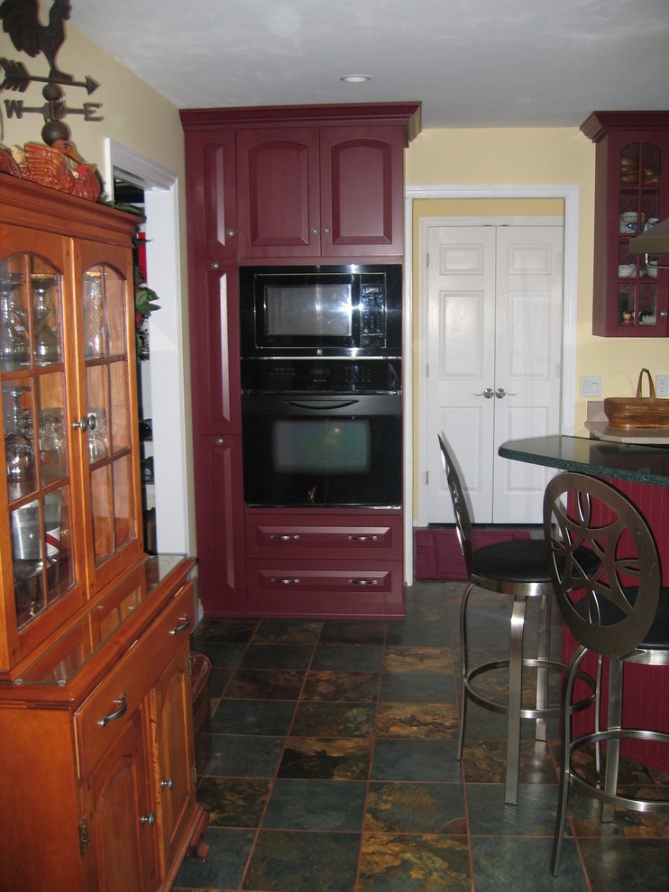 This is an example of a mid-sized traditional l-shaped eat-in kitchen in St Louis with a double-bowl sink, glass-front cabinets, red cabinets, quartz benchtops, black appliances, slate floors and with island.