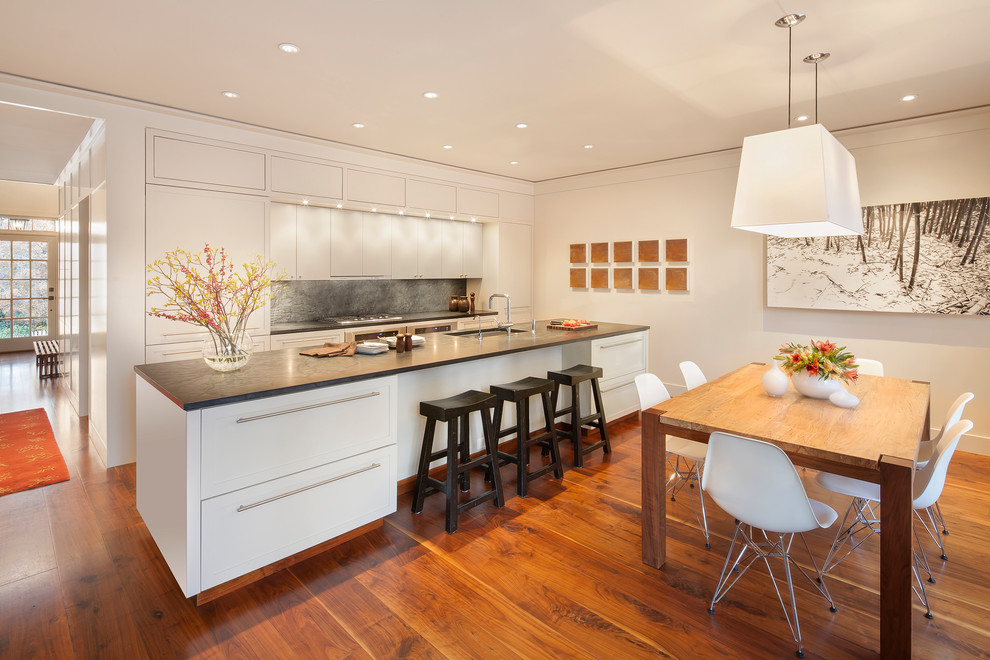Mid-sized contemporary galley eat-in kitchen in Atlanta with flat-panel cabinets, white cabinets, an undermount sink, soapstone benchtops, grey splashback, stone slab splashback, stainless steel appliances, medium hardwood floors, with island and brown floor.