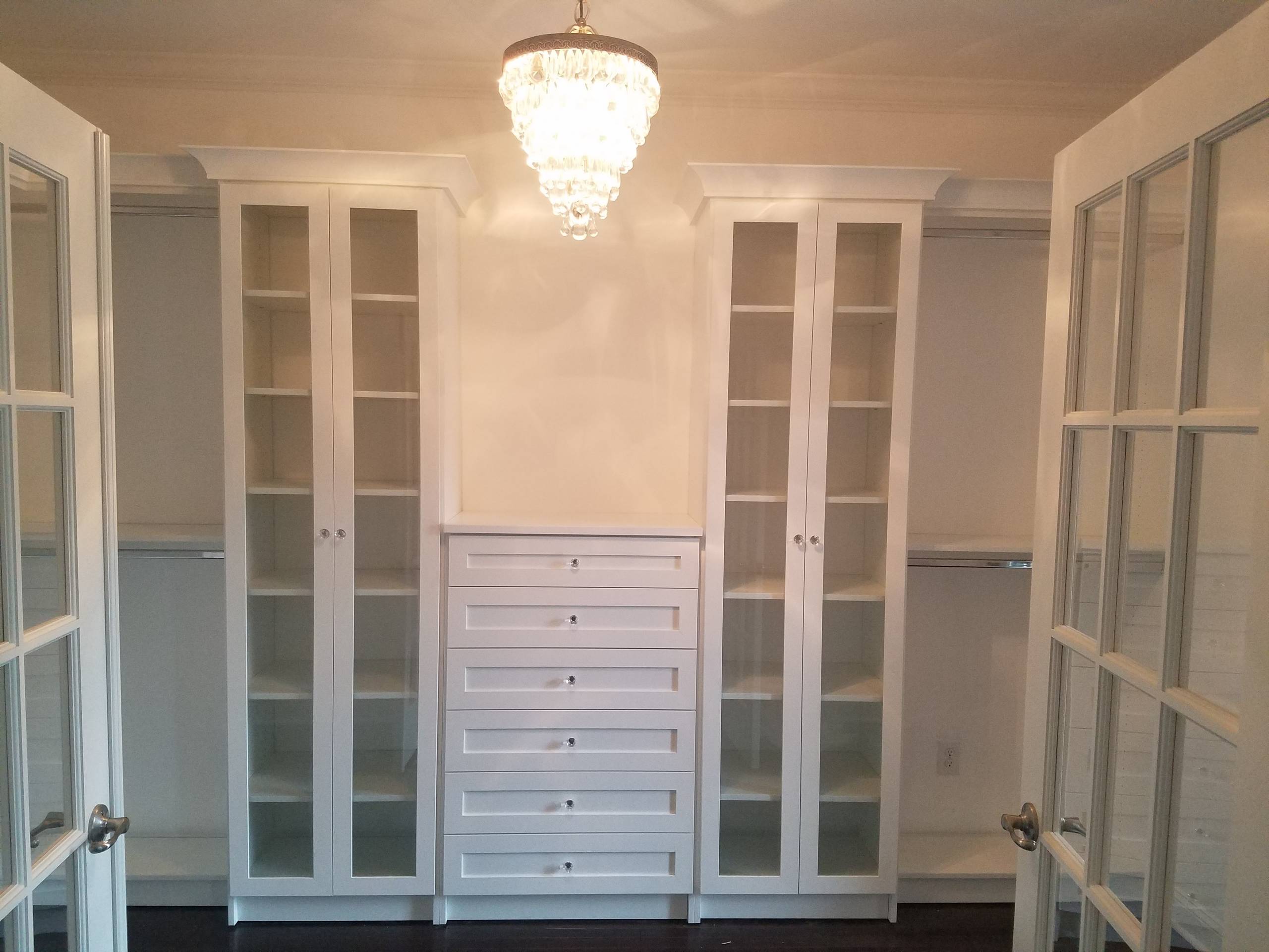 White walk in closet with shaker style drawer fronts and crown molding.  Also includes glass cabinets