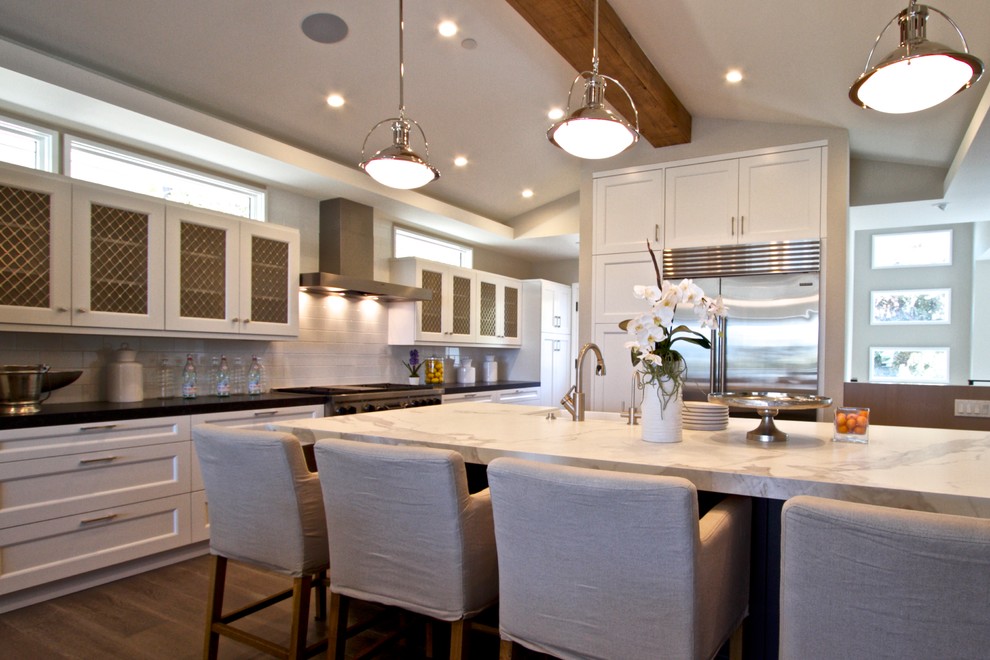 Example of a large transitional single-wall dark wood floor eat-in kitchen design in Orange County with a farmhouse sink, shaker cabinets, white cabinets, marble countertops, white backsplash, subway tile backsplash, stainless steel appliances and an island