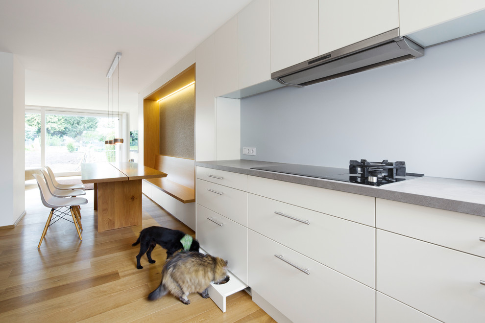 Photo of a mid-sized modern open plan kitchen in Other with flat-panel cabinets, white cabinets, grey splashback, medium hardwood floors and no island.