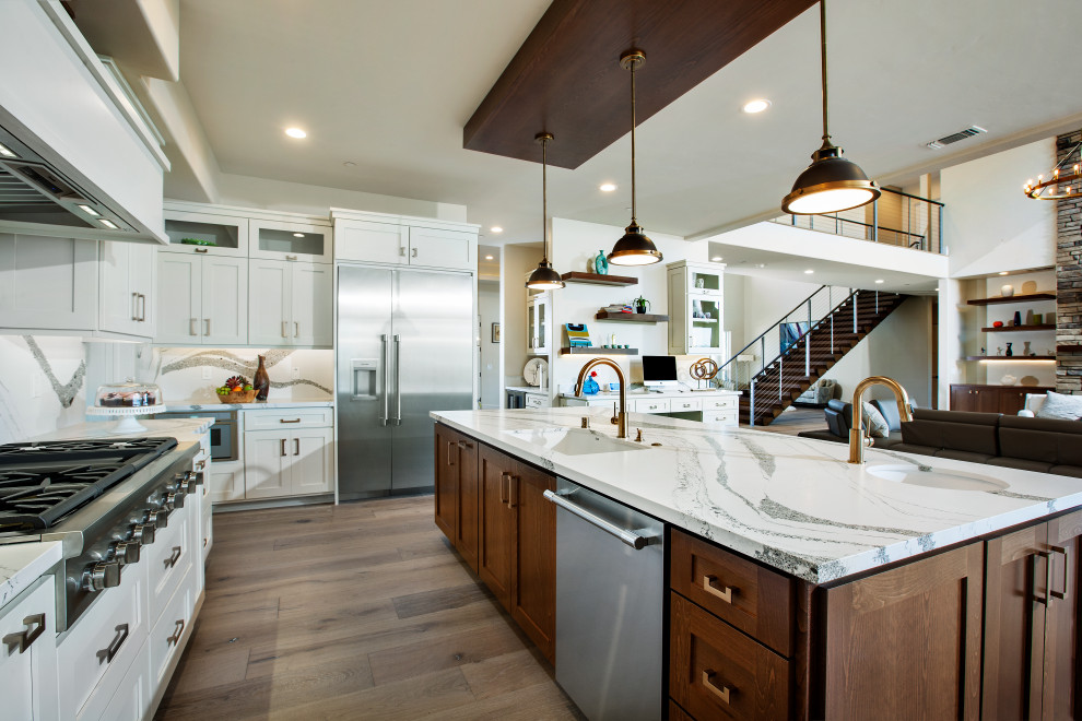 Inspiration for a large transitional l-shaped eat-in kitchen in Sacramento with an undermount sink, shaker cabinets, white cabinets, quartz benchtops, white splashback, engineered quartz splashback, stainless steel appliances, light hardwood floors, with island, brown floor and white benchtop.
