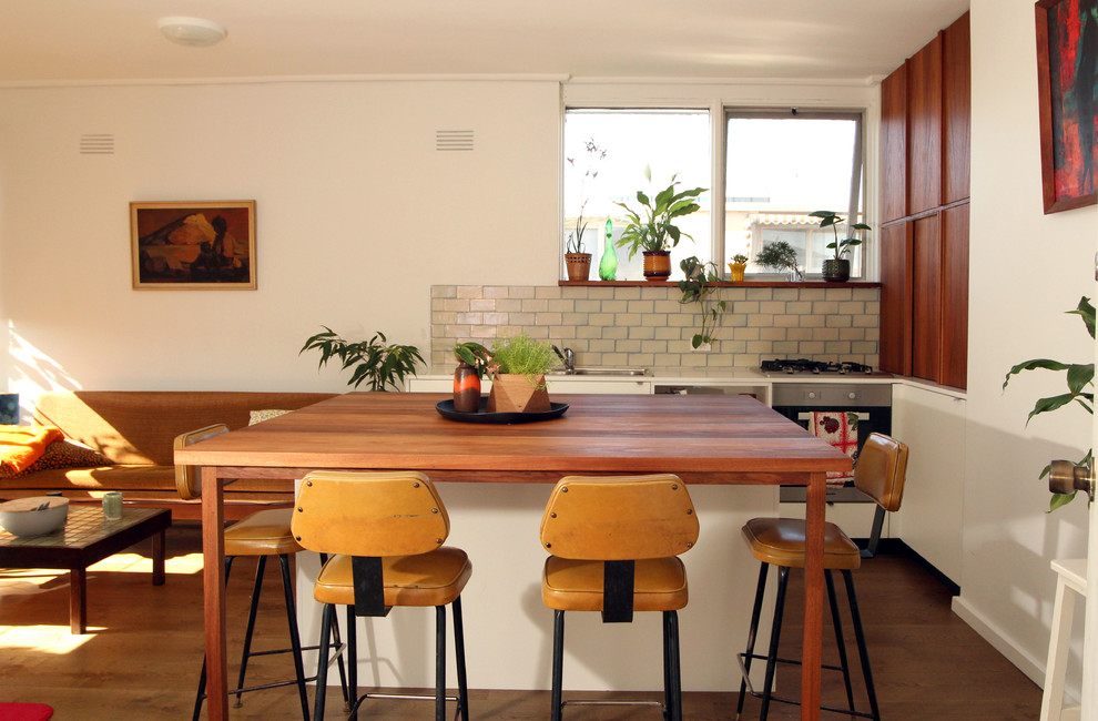 Photo of a small midcentury single-wall open plan kitchen in Melbourne with a drop-in sink, flat-panel cabinets, dark wood cabinets, quartz benchtops, white splashback, ceramic splashback, stainless steel appliances, dark hardwood floors and with island.