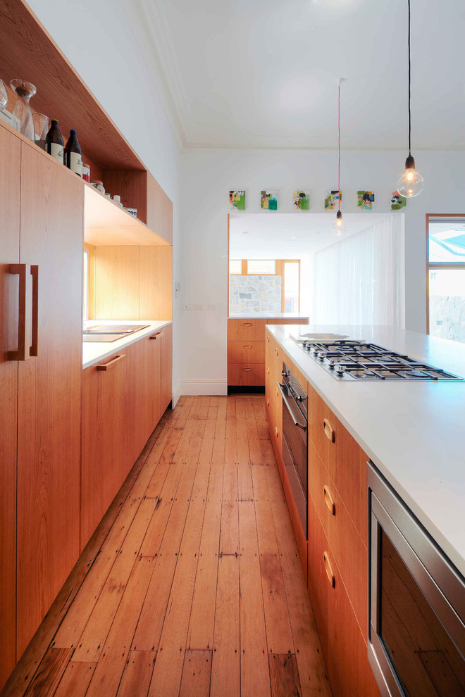 This is an example of a mid-sized modern galley eat-in kitchen in Sydney with flat-panel cabinets, medium wood cabinets, medium hardwood floors, with island, a drop-in sink, quartz benchtops and stainless steel appliances.