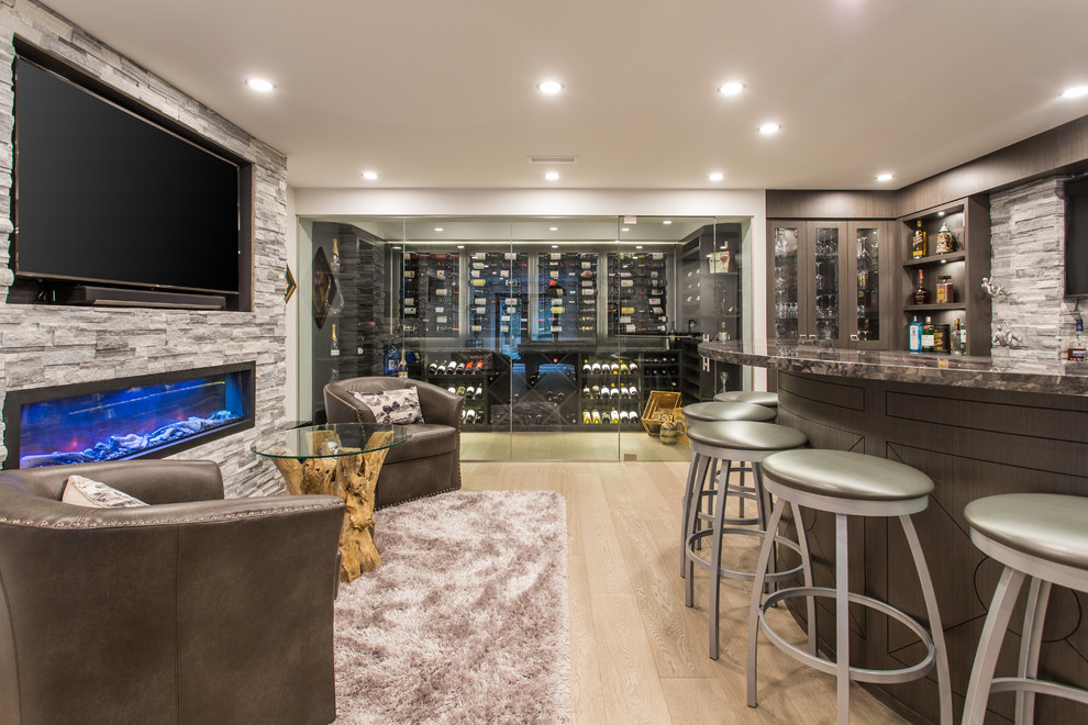 Inspiration for a large transitional u-shaped seated home bar in Vancouver with an undermount sink, brown cabinets, marble benchtops, grey splashback, stone tile splashback, medium hardwood floors, beige floor and black benchtop.
