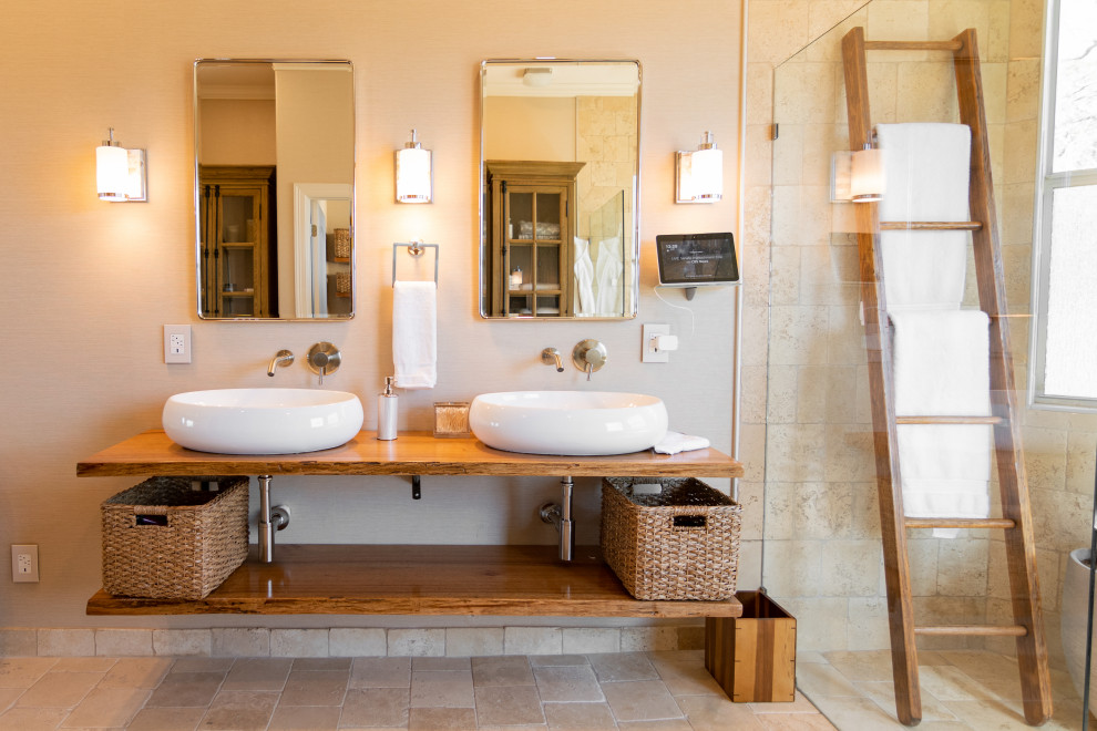 Inspiration for a large mediterranean master wet room bathroom in Austin with open cabinets, distressed cabinets, a two-piece toilet, beige tile, travertine, beige walls, travertine floors, a vessel sink, wood benchtops, beige floor, a hinged shower door and brown benchtops.