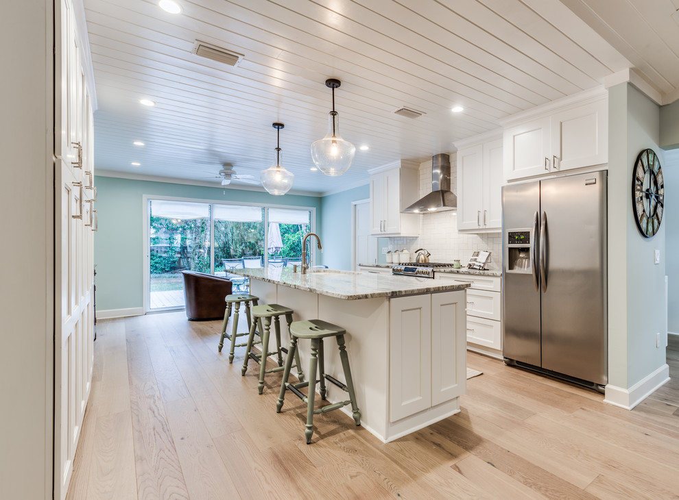 Design ideas for a beach style galley separate kitchen in Jacksonville with shaker cabinets, white cabinets, white splashback, subway tile splashback, stainless steel appliances, light hardwood floors, with island and beige floor.