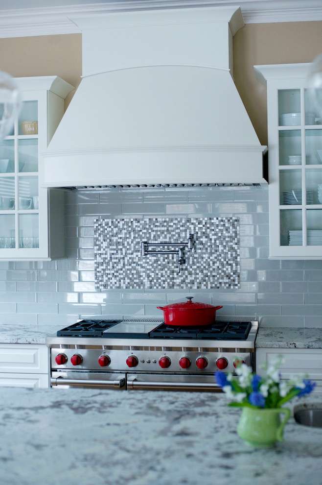 Example of a mid-sized transitional l-shaped medium tone wood floor open concept kitchen design in Atlanta with a farmhouse sink, raised-panel cabinets, white cabinets, granite countertops, gray backsplash, glass tile backsplash, stainless steel appliances and an island