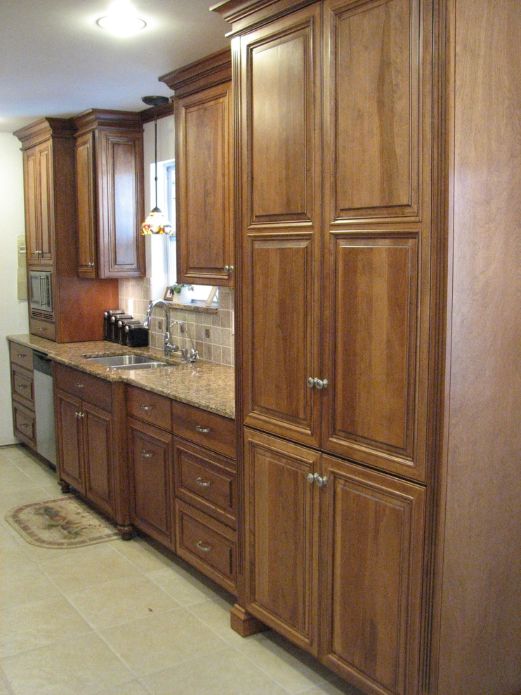 Photo of a mid-sized transitional galley open plan kitchen in Jacksonville with an undermount sink, raised-panel cabinets, dark wood cabinets, granite benchtops, beige splashback, stone tile splashback, stainless steel appliances, ceramic floors and no island.