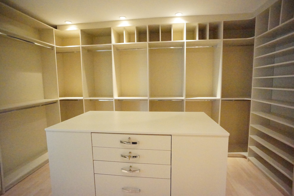This is an example of a large traditional gender-neutral walk-in wardrobe in Miami with flat-panel cabinets, white cabinets and light hardwood floors.