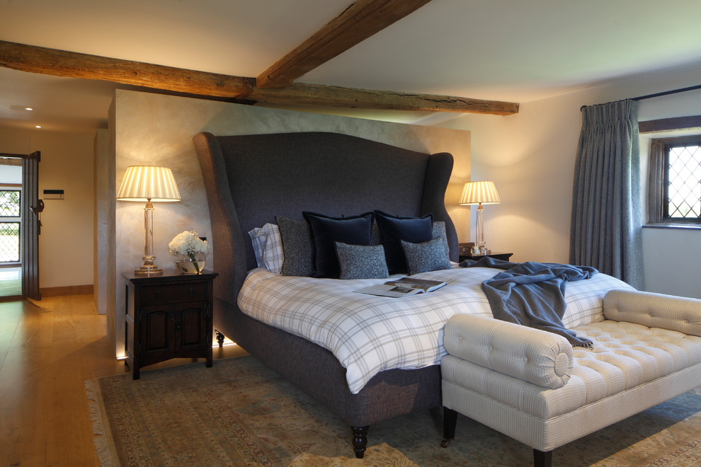 This is an example of a country bedroom in London with beige walls, medium hardwood floors and brown floor.
