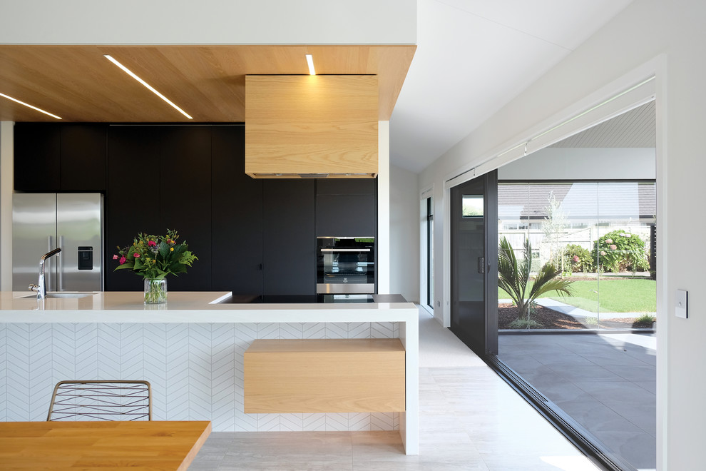 Inspiration for a mid-sized midcentury galley open plan kitchen in Other with a single-bowl sink, flat-panel cabinets, black cabinets, solid surface benchtops, white splashback, ceramic splashback, stainless steel appliances, ceramic floors, with island, grey floor and white benchtop.