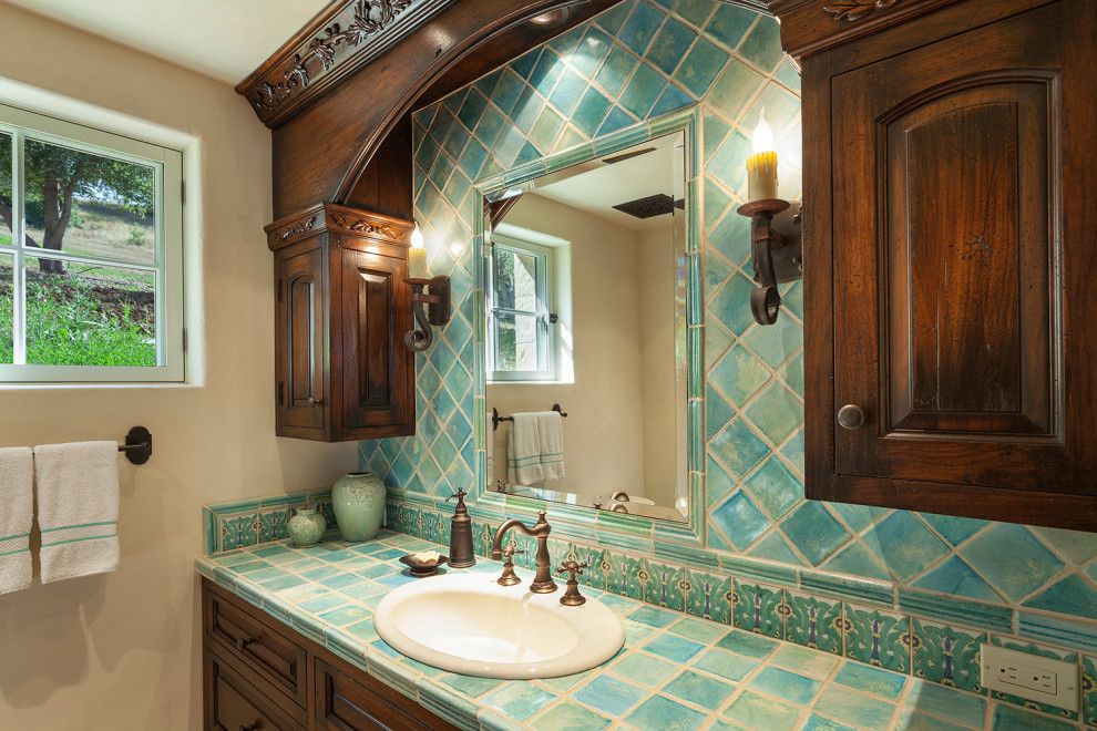 This is an example of a mid-sized country bathroom in Santa Barbara with raised-panel cabinets, distressed cabinets, an alcove shower, blue tile, ceramic tile, beige walls, travertine floors, a drop-in sink, limestone benchtops, beige floor, a hinged shower door, beige benchtops, a shower seat, a single vanity, a built-in vanity and vaulted.