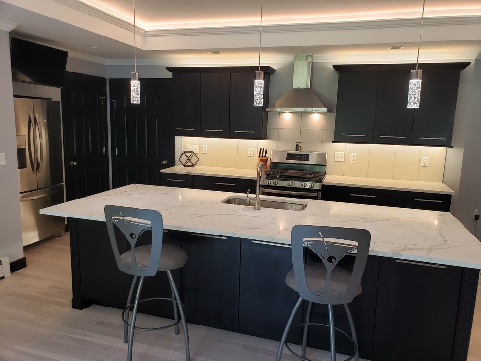 Photo of a modern galley open plan kitchen in Other with an undermount sink, flat-panel cabinets, black cabinets, quartzite benchtops, white splashback, porcelain splashback, stainless steel appliances, light hardwood floors, with island, white floor and white benchtop.
