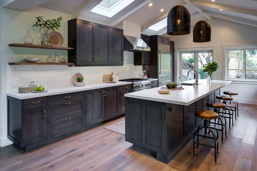 Inspiration for a transitional galley open plan kitchen in San Francisco with an undermount sink, shaker cabinets, white splashback, subway tile splashback, stainless steel appliances, with island, brown floor, white benchtop, grey cabinets, quartz benchtops and light hardwood floors.