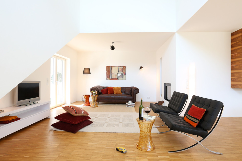 This is an example of a large contemporary open concept living room in Frankfurt with white walls, medium hardwood floors, a standard fireplace, a plaster fireplace surround and a freestanding tv.