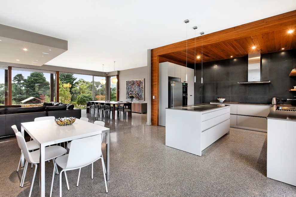 This is an example of a mid-sized contemporary u-shaped eat-in kitchen in Melbourne with a drop-in sink, flat-panel cabinets, white cabinets, quartz benchtops, grey splashback, porcelain splashback, stainless steel appliances, concrete floors and with island.
