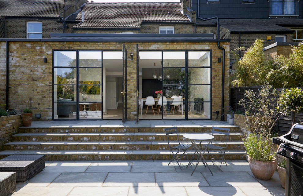 Inspiration for a mid-sized contemporary backyard patio in London with natural stone pavers.