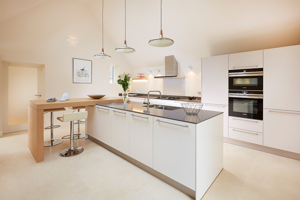 This is an example of a large contemporary single-wall eat-in kitchen in Oxfordshire with an integrated sink, flat-panel cabinets, white cabinets, solid surface benchtops, glass sheet splashback, stainless steel appliances, porcelain floors and with island.