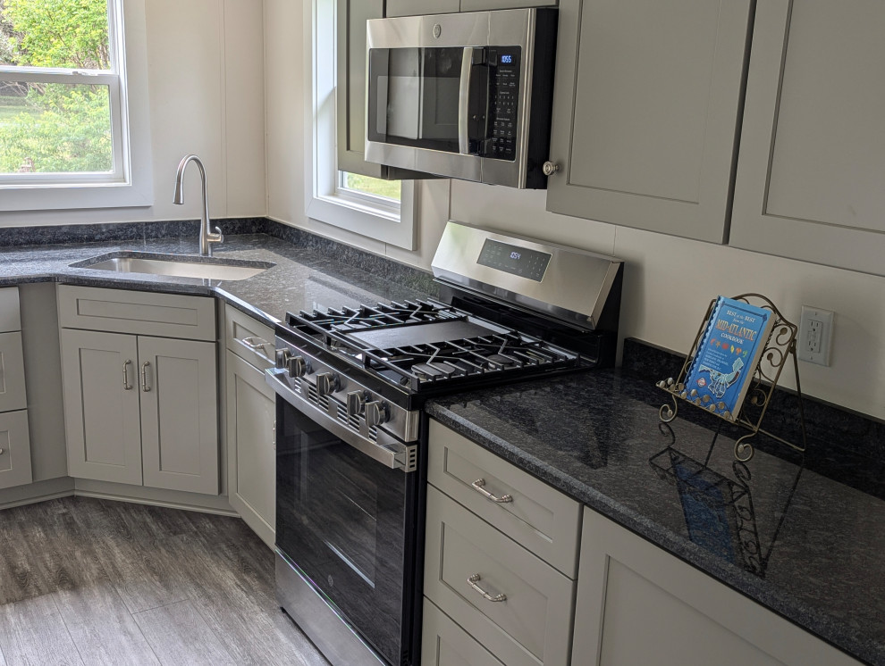 Small transitional l-shaped gray floor enclosed kitchen photo with a single-bowl sink, flat-panel cabinets, gray cabinets, granite countertops, stainless steel appliances and black countertops