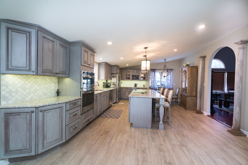 Photo of a large traditional l-shaped open plan kitchen in DC Metro with an undermount sink, beaded inset cabinets, distressed cabinets, granite benchtops, green splashback, porcelain splashback, stainless steel appliances, medium hardwood floors, with island, brown floor and multi-coloured benchtop.