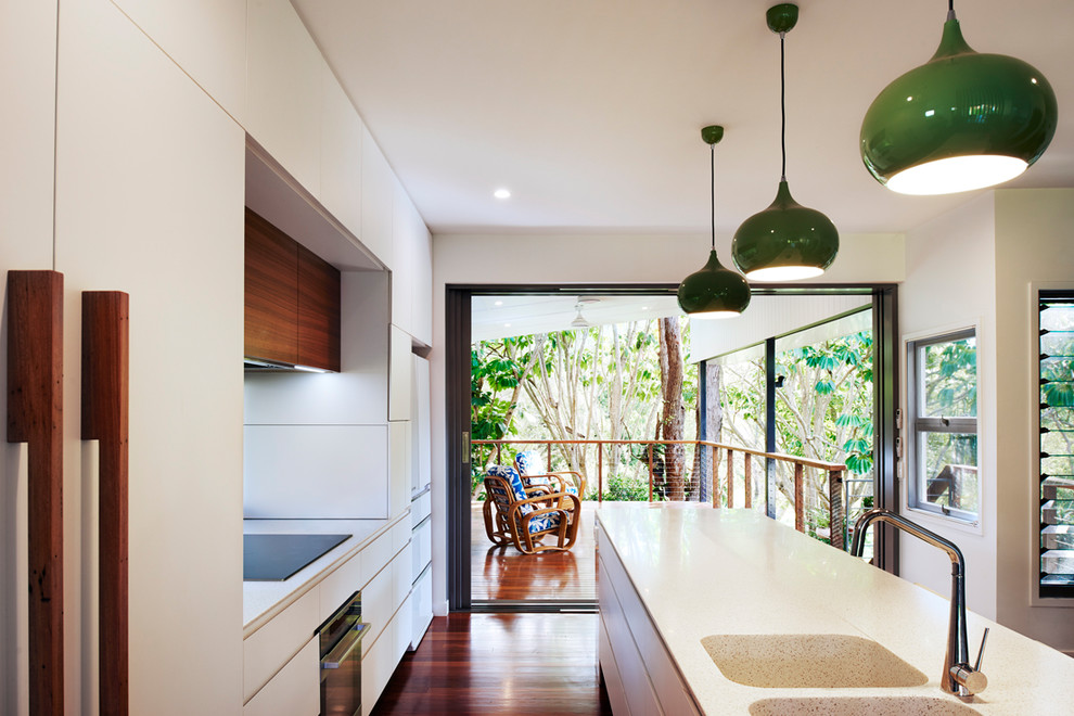 Inspiration for a galley eat-in kitchen in Brisbane with an integrated sink, white cabinets, solid surface benchtops, window splashback, white appliances, dark hardwood floors, with island and white benchtop.