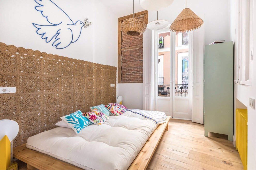 Eclectic bedroom in Madrid with white walls and light hardwood floors.
