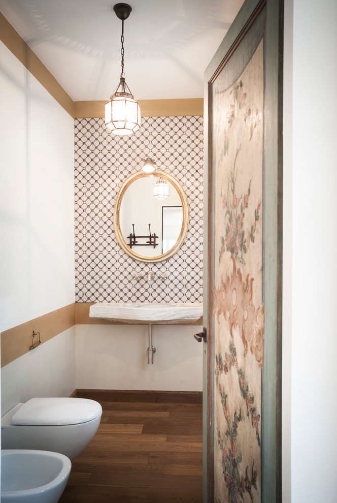 This is an example of a mid-sized traditional bathroom in Milan with a wall-mount toilet, beige tile, white tile, multi-coloured walls, dark hardwood floors, a wall-mount sink and brown floor.