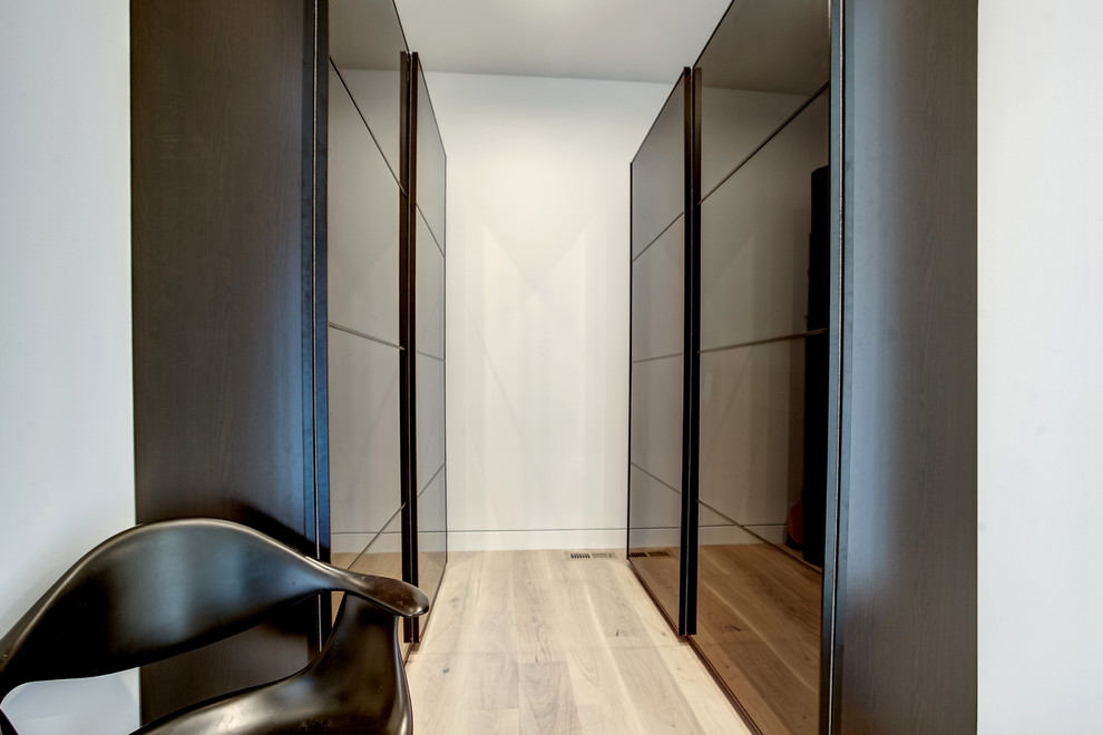 Mid-sized modern gender-neutral walk-in wardrobe in Grand Rapids with glass-front cabinets, dark wood cabinets and light hardwood floors.
