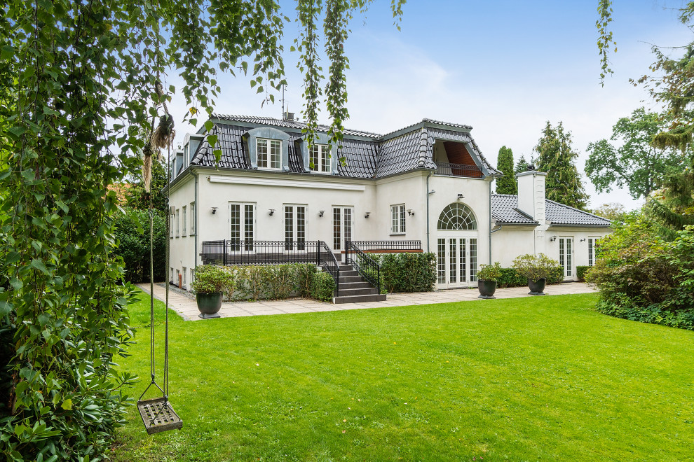 This is an example of a traditional two-storey white house exterior in Copenhagen with a hip roof and a tile roof.