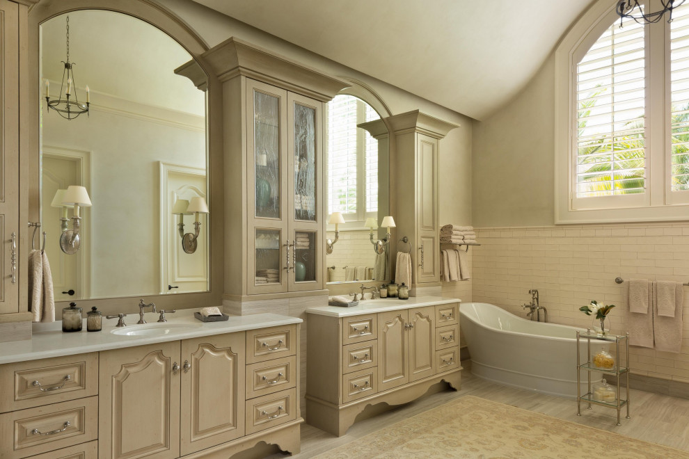 This is an example of a master bathroom in Miami with raised-panel cabinets, beige cabinets, a freestanding tub, white tile, subway tile, grey walls, an undermount sink, grey floor, white benchtops, a double vanity, a built-in vanity and vaulted.