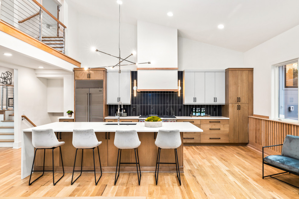 Inspiration for a contemporary open plan kitchen in Atlanta with an undermount sink, flat-panel cabinets, medium wood cabinets, black splashback, stainless steel appliances, light hardwood floors, with island, white benchtop and vaulted.