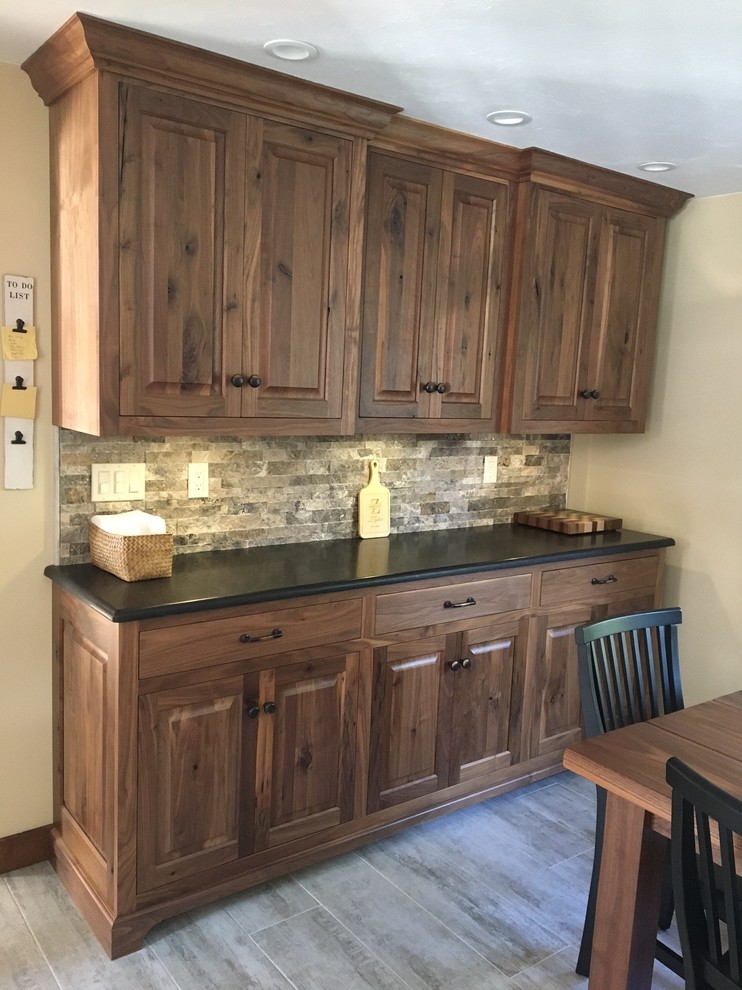 This is an example of a large country l-shaped eat-in kitchen in Boston with an undermount sink, raised-panel cabinets, dark wood cabinets, granite benchtops, grey splashback, subway tile splashback, stainless steel appliances, cement tiles, with island and white floor.