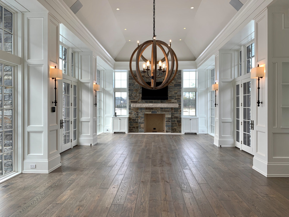 Example of a huge trendy medium tone wood floor, brown floor, vaulted ceiling and wood wall family room design in Chicago with white walls, a standard fireplace, a stone fireplace and a wall-mounted tv